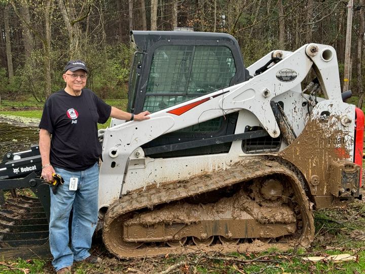 A volunteer stands beside a mud-covered tracked loader