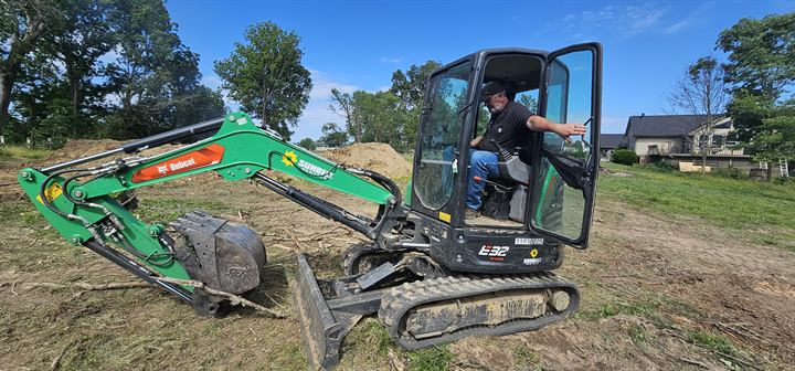 A volunteer runs a mini excavator on a cleared lot