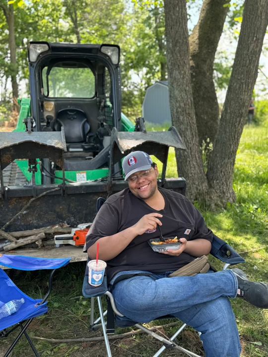 A volunteer takes a lunch break beside a skid steer